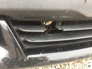 Close-up of a black car’s front bumper and grille, showing minor scratches and dust. Some stones or gravel are scattered beneath. Perfect for a Free auto body repair estimate online or to request a collision repair quote.