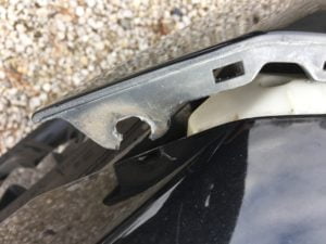 A close-up of a broken plastic car part with a jagged edge, resting above a black surface. Gravel is visible in the background—perfect for illustrating damage when requesting a Free auto body repair estimate online.