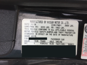 A close-up of a vehicle information sticker from Nissan Motor Co., showing manufacturing details, weight ratings, VIN, and specs like color and engine codes. Some info is blacked out—ideal for those seeking a collision repair quote or a free auto body repair estimate online.