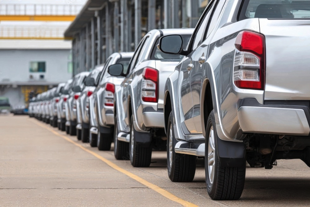 A row of silver pickup trucks is parked beside a building, all facing the same direction on a concrete lot.
